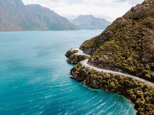 Nelson Car Rental vehicle driving along a scenic coastal highway in Nelson, New Zealand